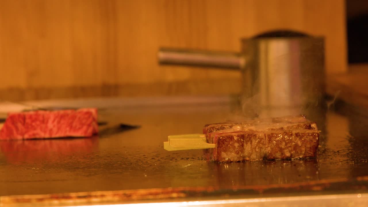 熱い鉄板の鉄板焼きグリルで焼かれる、プレミアムな霜降り牛肉のステーキのクローズアップショット。