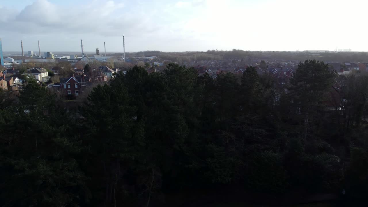 Vista aerea panoramica sugli alberi del parco verso un paesaggio urbano industriale con grattacielo blu, Merseyside, Inghilterra