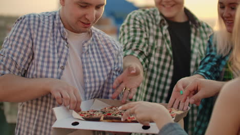 young people celebrate a friends birthday. they eat hot pizza and drink beer and enjoy a summer evening on the roof.