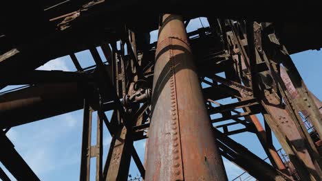 Intricate,-rusted-exterior-of-an-old-industrial-structure,-featuring-a-large-cylindrical-pipesurrounded-by-crisscrossing-metal-beams