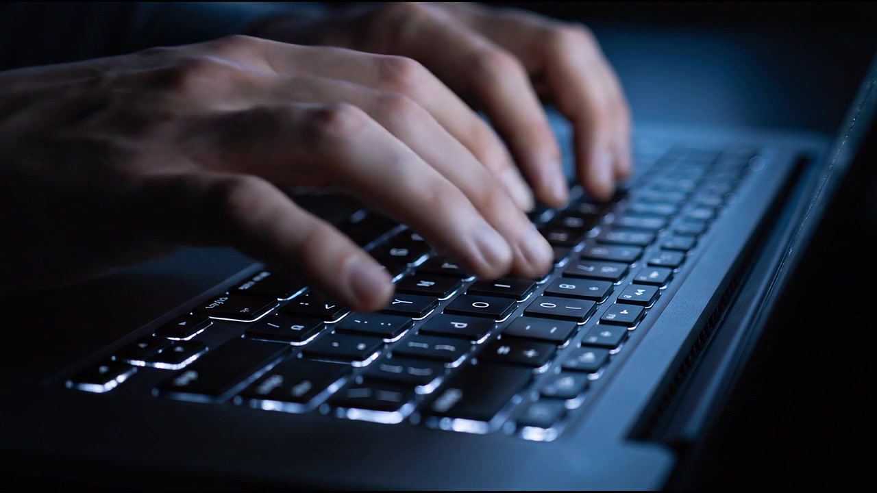 Closeup of fingers typing on glowing laptop keyboard during late night computer work session