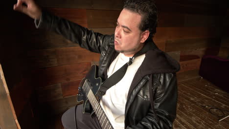 young hispanic male strumming electric guitar at a studio in slow motion