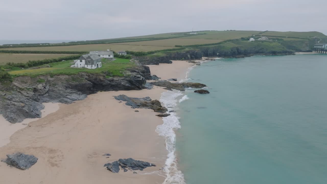 Houses on low sea cliffs next to clean sandy beach with blue water. Mother Ivey's Bay, Cornwall, UK.