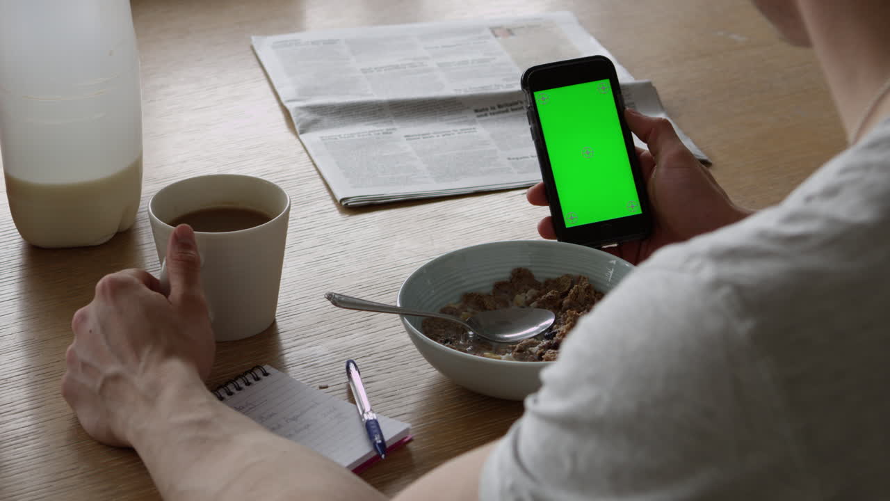 hombre usando un teléfono inteligente con pantalla verde y tomando el desayuno