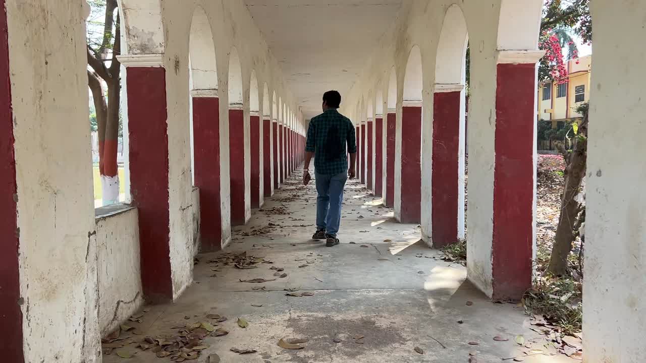 Shot of male walking through haunted corridor with series of arched openings of a building.