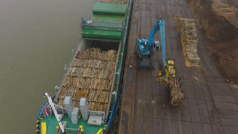 aerial establishing view of wood terminal crane loading timber into the cargo ship, port of liepaja , lumber log export, overcast day with fog and mist, birdseye drone shot