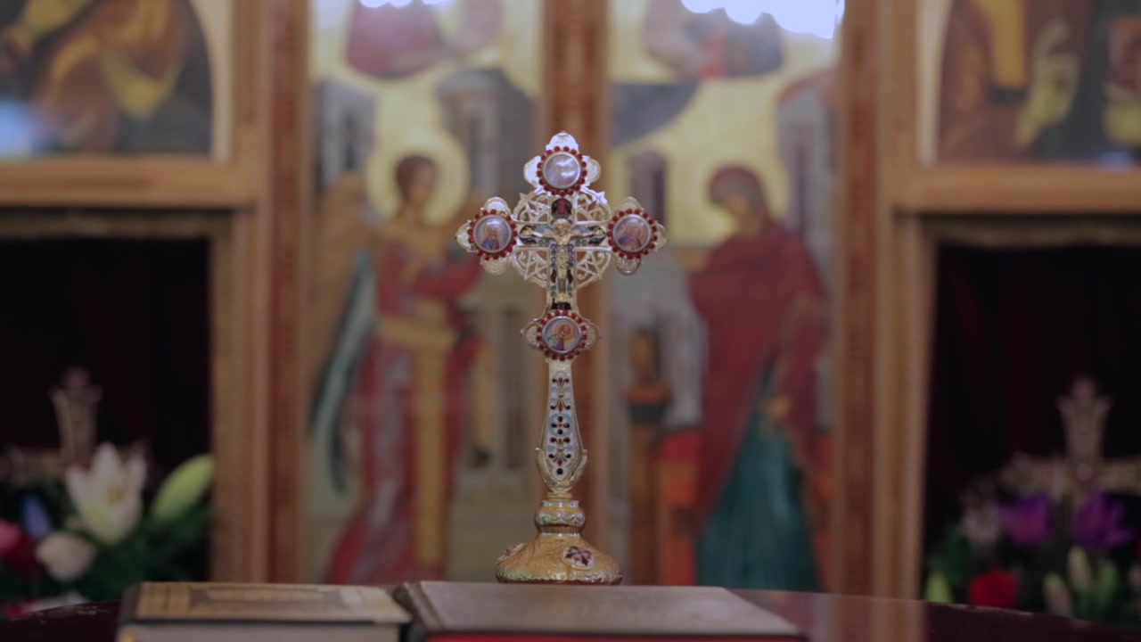Parallax shot of an ornate cross inside an Orthodox church, with religious icons in the background