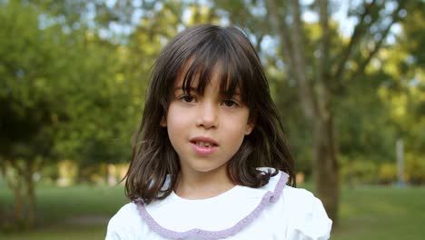 linda y pensativa niña de pelo negro parada en el parque de la ciudad