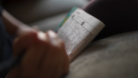 Close-up-of-a-page-in-a-Sudoku-puzzle-book-as-a-woman's-hand-fills-in-the-numbers