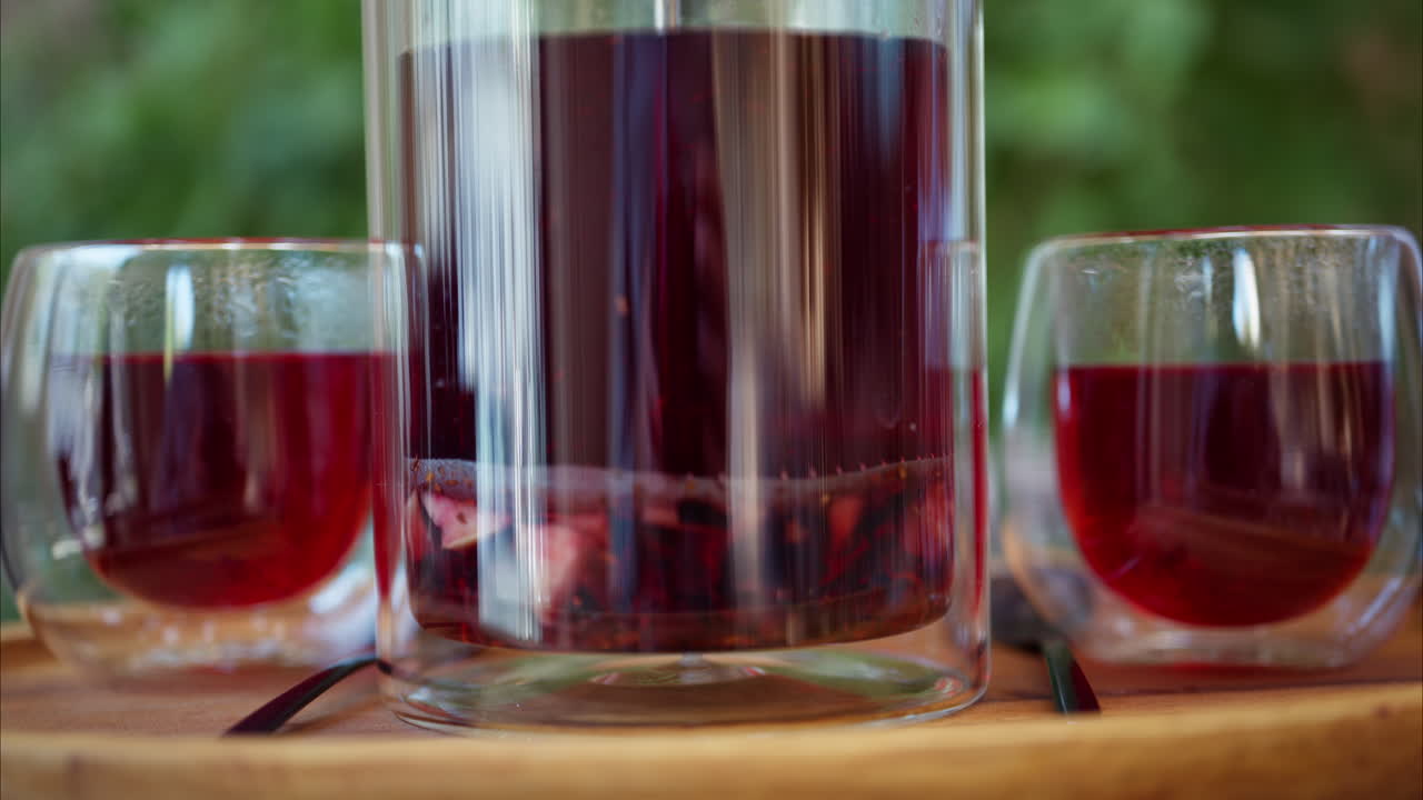 Close up of an infuser teapot with two cups of fruit tea on a table at a terrace