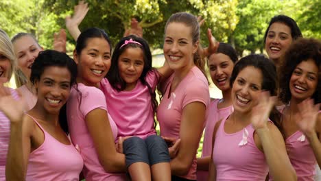 mujeres felices en rosa para la concientización sobre el cáncer de mama en el parque saludando a la cámara