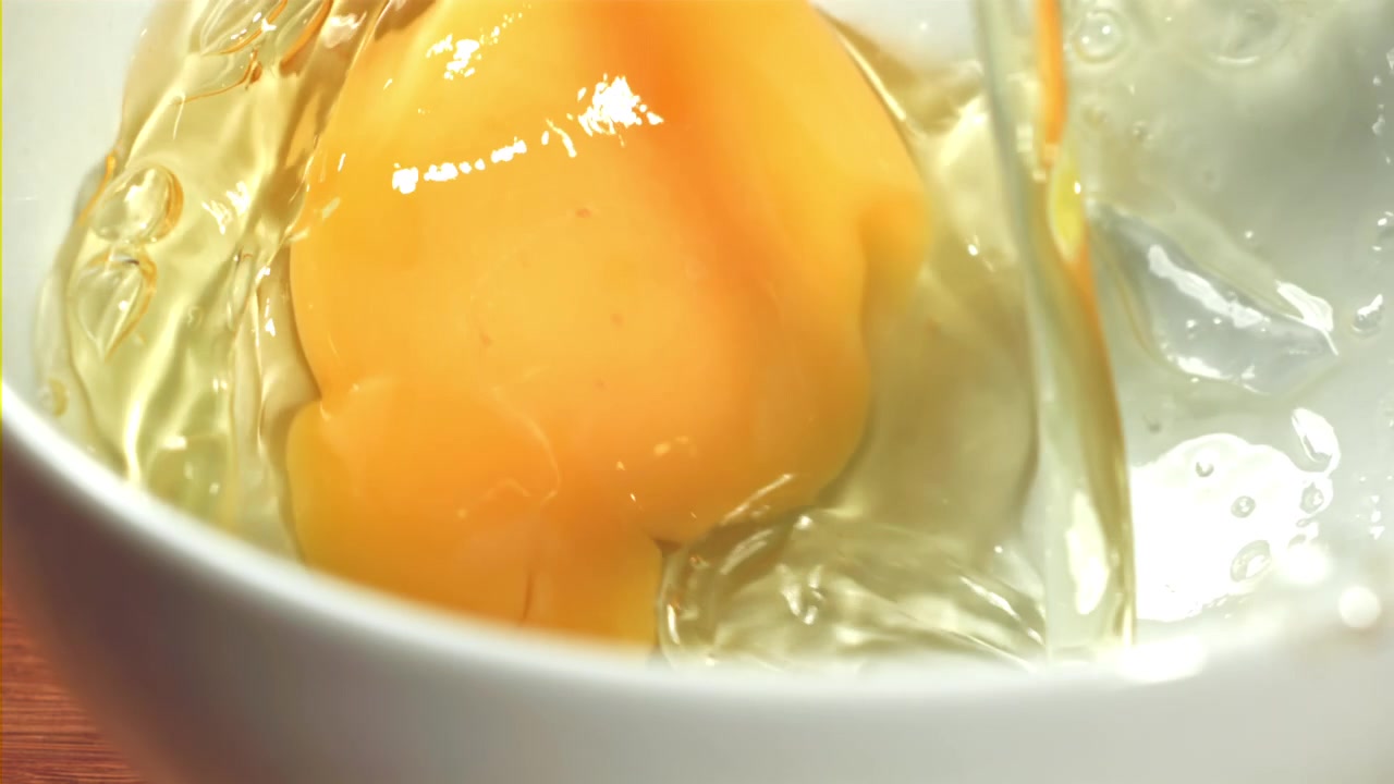 Ferskt egg knekkes og helles i en hvit bolle i sakte film