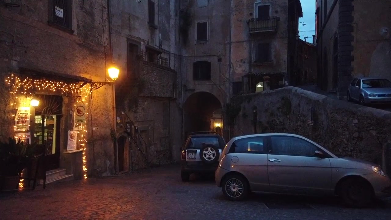 Bracciano è una città vicino a Roma. Ha un centro storico. L'inquadratura mostra una strada illuminata da poche luci
