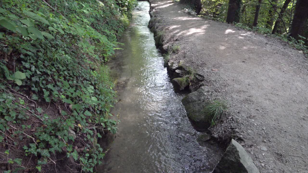 A man-made irrigation canal next to a hiking trail in a forest. Irrigation canals are used to transport water from a source to various users.
