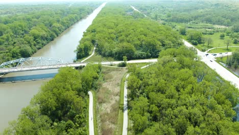 Aerial-view-over-cyclists-on-a-bike-trail-next-to-a-busy-rural-road-in-the-forest