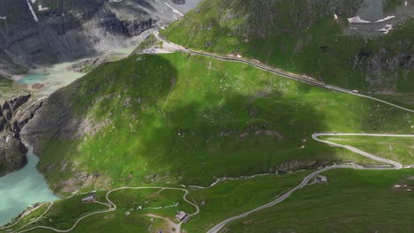 winding road through green alpine mountains under a partly cloudy sky, aerial view