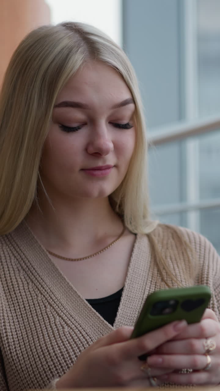 signora seduta con il telefono in mano, con l'aspetto riflessivo con il caffè sfocato sul tavolo e la vista sfocata della città fuori dalla finestra, atmosfera urbana pacifica, ambiente moderno, momento tranquillo in un caffè