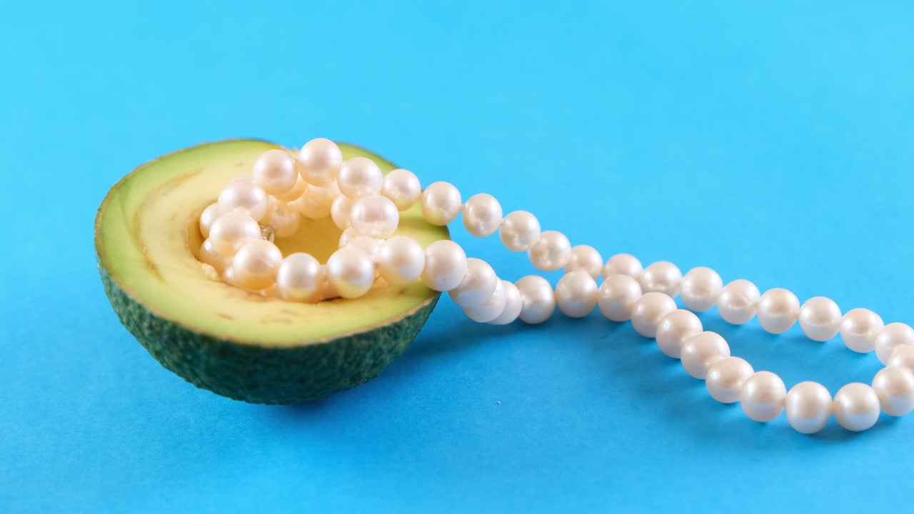medio fruto de aguacate fresco con perlas en fondo azul. diseño de alimentos de moda