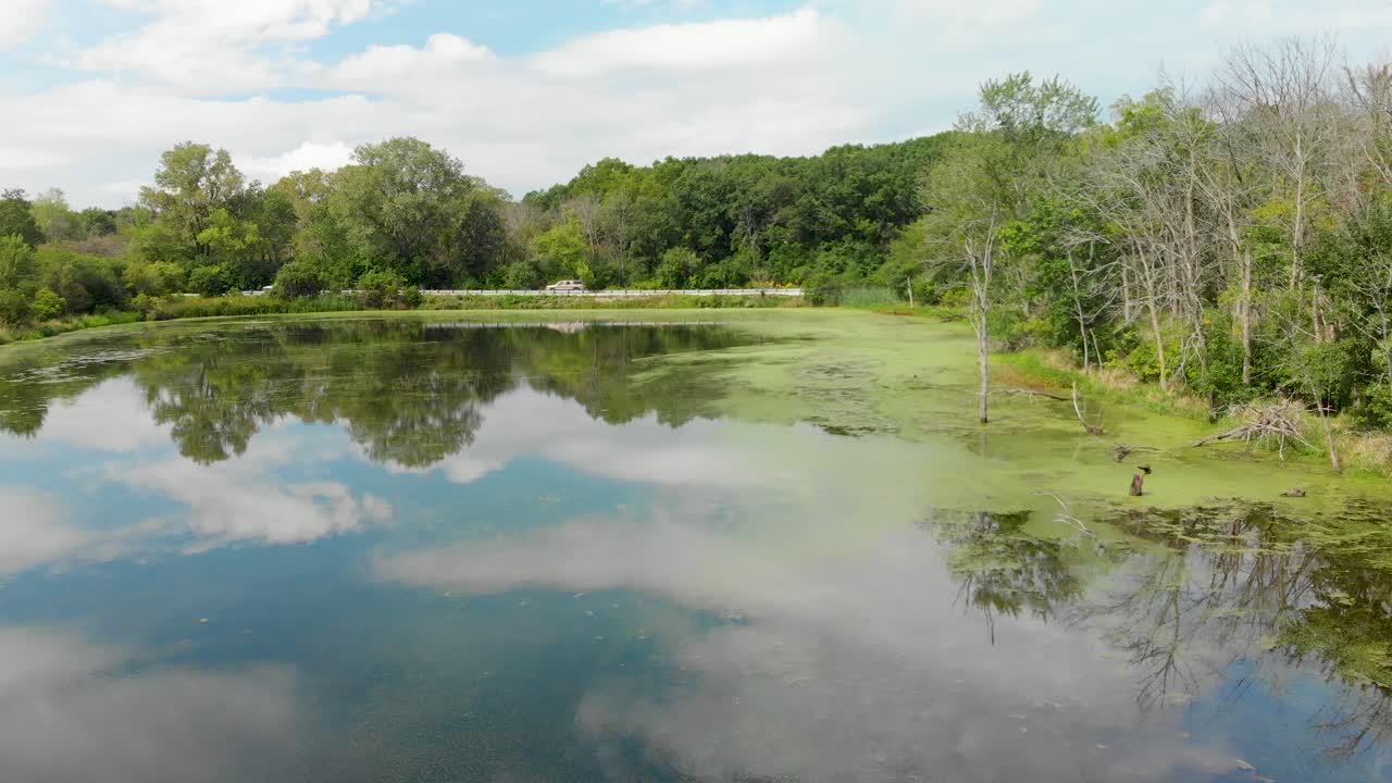 coches conduciendo por un camino de campo rural al lado de un lago lleno de algas izquierdo vuelo drone 4k