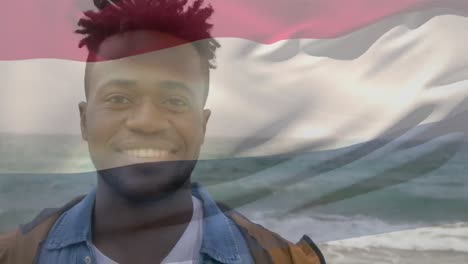 animación de la bandera nacional de los países bajos ondeando sobre un hombre afroamericano sonriente de pie en la playa