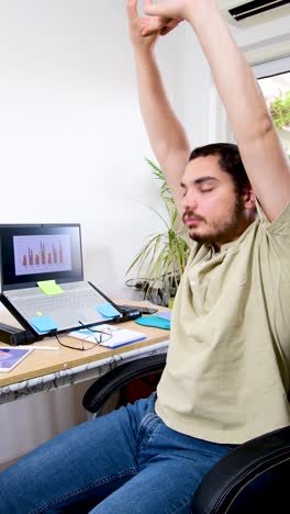 man working from home on computer in home office stretching at desk.