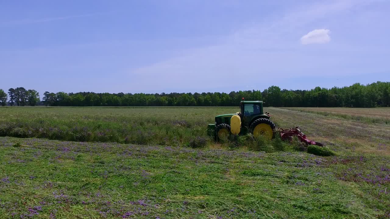 트랙터가 큰 하늘로 잔디를 자르면서 필드의 뒤로 드론 샷