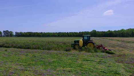 tiro de dron hacia atrás del campo mientras el tractor corta hierba con un gran cielo
