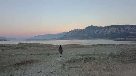 Forward-drone-shot-of-a-girl-walking-to-a-lake