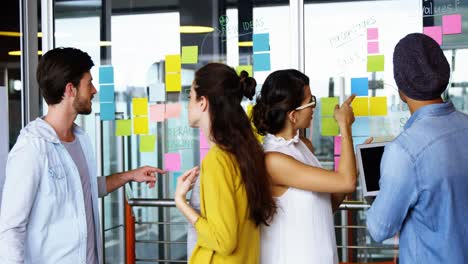Executives-discussing-over-sticky-notes-on-glass-wall