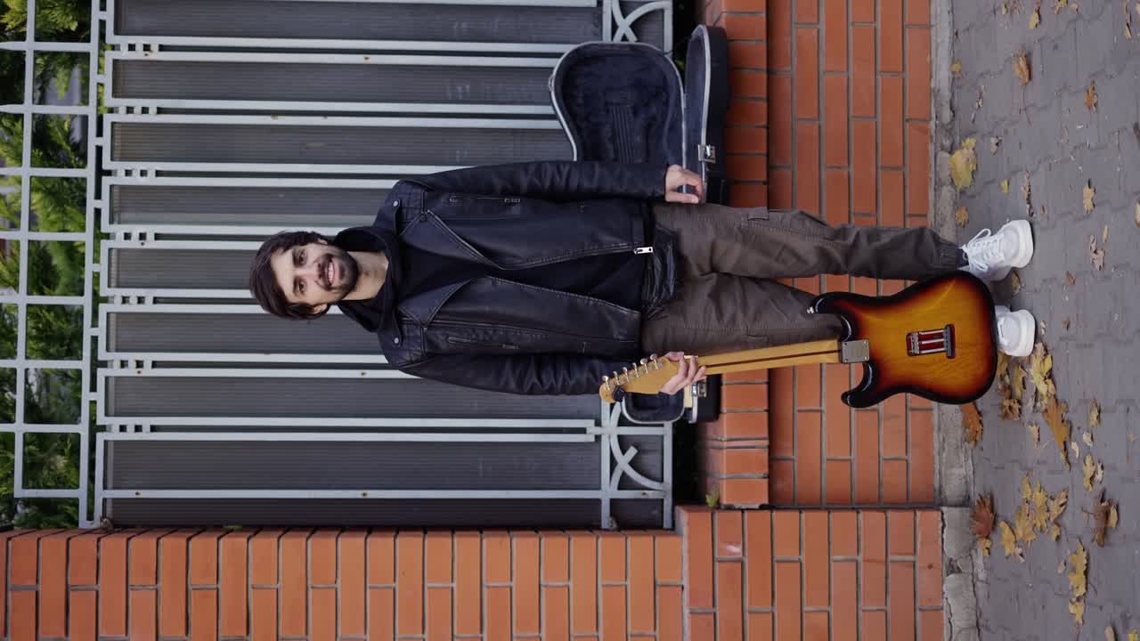 un tipo feliz sonriendo en la calle con una guitarra