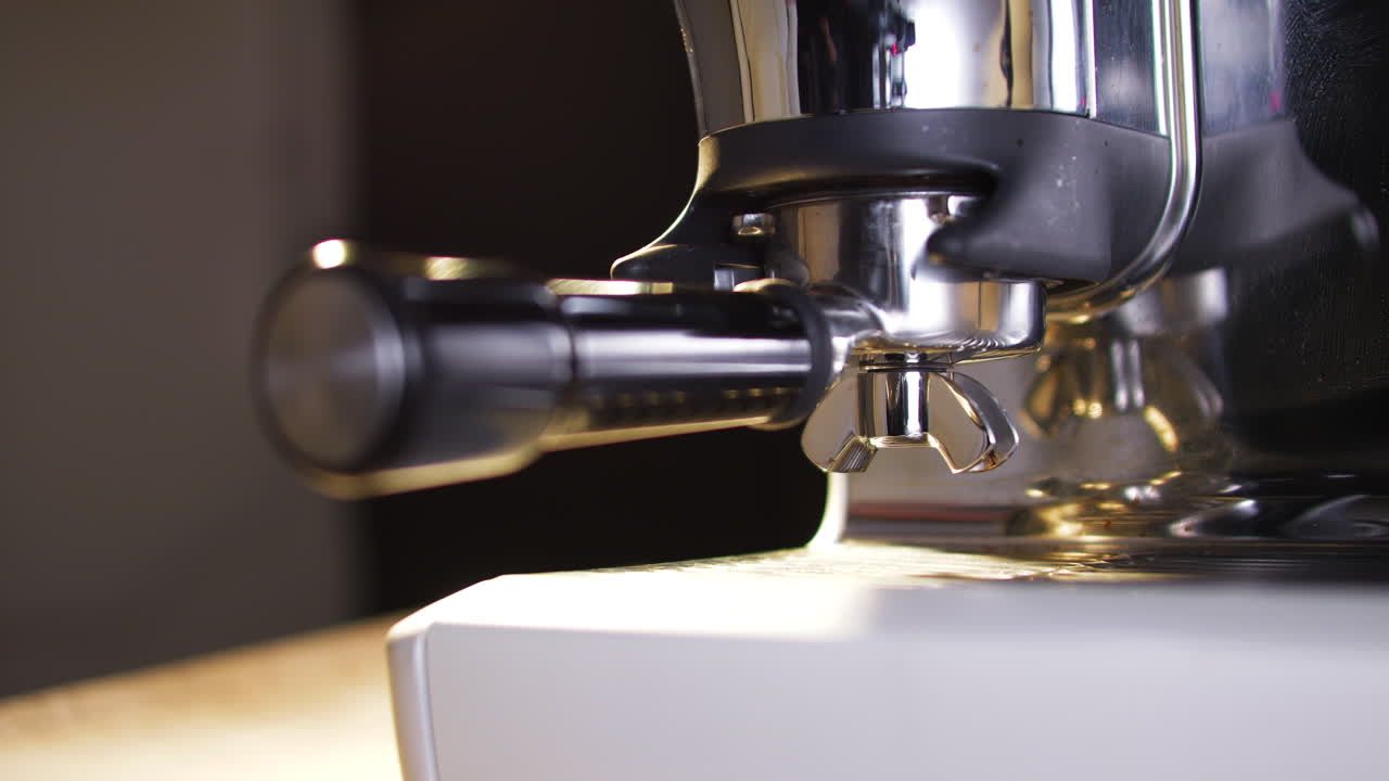 Close-up de barista removendo porta-filtro de moedor automático de café expresso após dosar café fresco. Movimento limpo e superfícies metálicas destacam o fluxo de trabalho e a preparação.