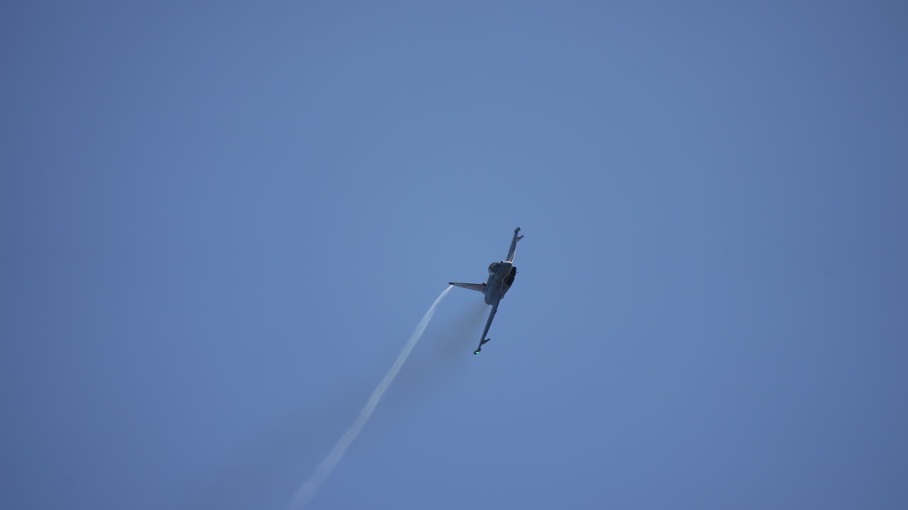 Military jet fighter flying toward camera while spinning in midair against clear sky
