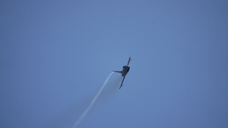 military jet fighter flying toward camera while spinning in midair against clear sky