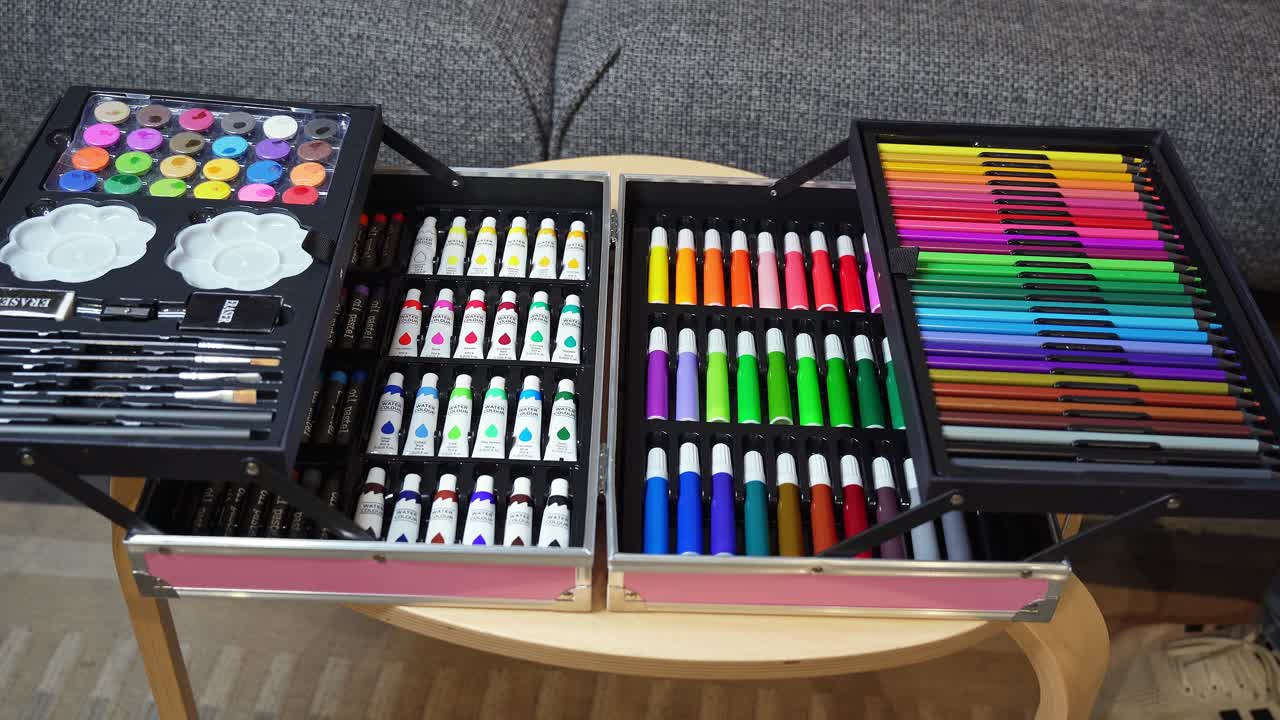 Closeup of an open art set with paints, brushes, pencils, and markers. Hand arranging supplies, symbolizing creativity, education, and design
