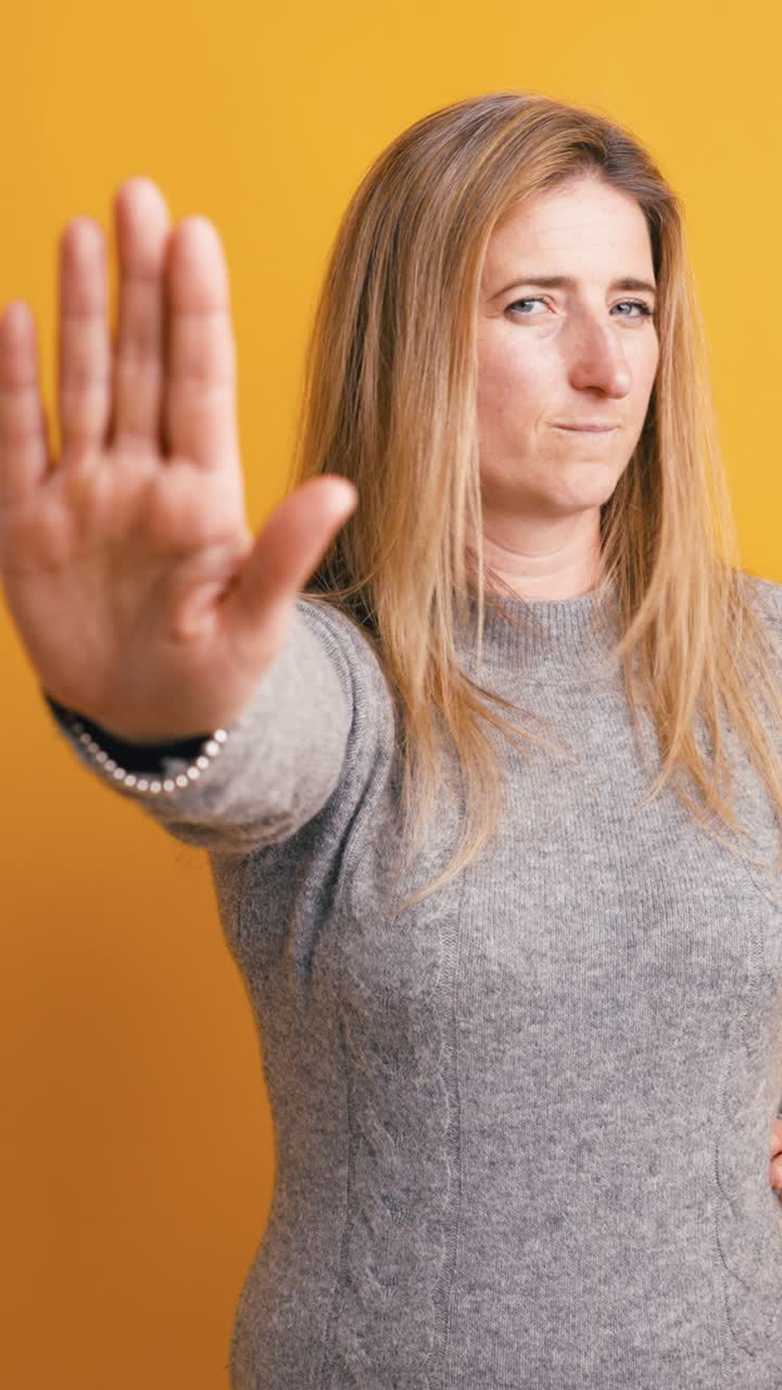 Woman Gesturing Stop with Hand Against Yellow Background