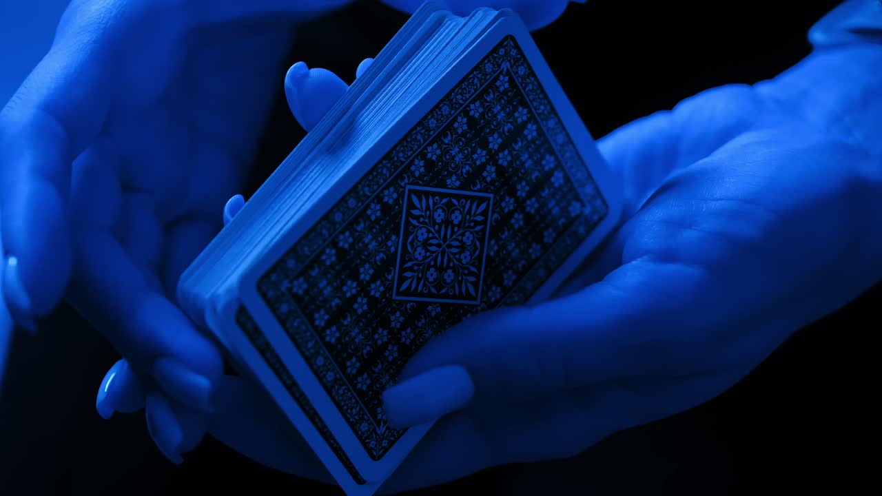 Stylized card trick by female hands lit in blue light, evoking calm precision