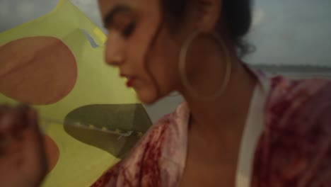 A-closeup-of-a-young-woman-wearing-large-golden-earrings-while-holding-a-yellow-kite-at-the-beach