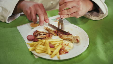 man's hands cut a slice of roasted chicken on a plate with french fries