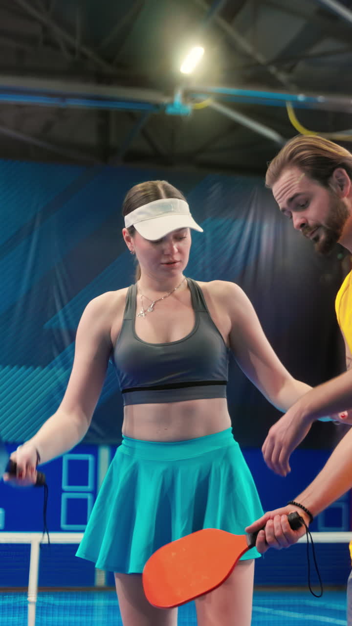 A man teaching a woman how to play pickleball in an inside court. Vertical