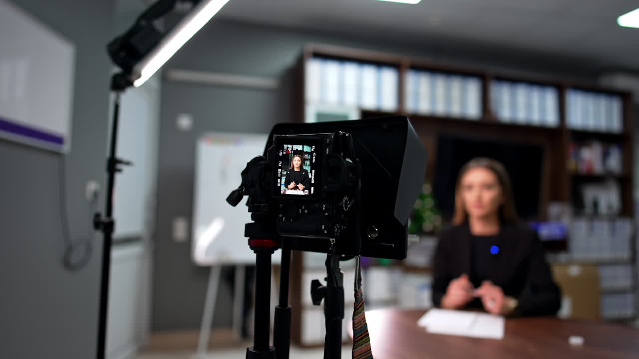 Video footage of a blog in the office. Female speaker talks to camera standing on tripod in front of her.