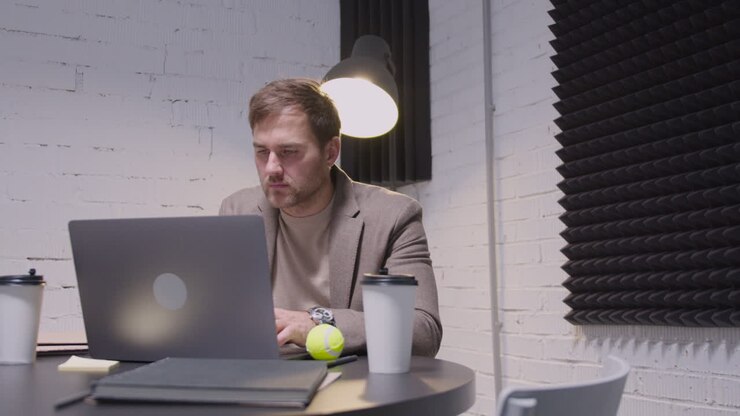 Geschäftsmann tippt am Laptop und spielt dann mit einem Tennisball, während er am Tisch im Sitzungssaal sitzt