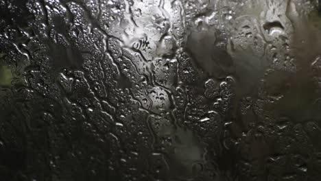 Lloviendo-En-La-Ventana-De-Un-Auto-Con-Las-Gotas-De-Lluvia-Cayendo,-Bosque-En-El-Fondo