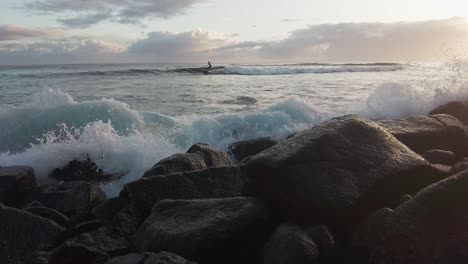 splashing waves hits shore, surfer in background, slow motion