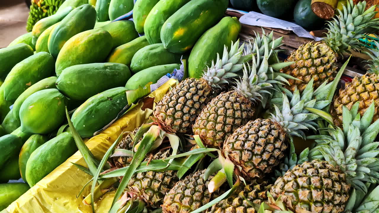 A colorful close-up shows an abundant pile of fresh green papayas and whole pineapples for sale at a rustic outdoor fruit stall, showcasing the local produce of Sri Lanka