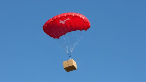 a bright red parachute gently descending with a box amidst clear blue skies, showcasing a unique airborne delivery system in action