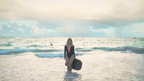 a girl stands in the ocean water in the swimming suit in the dusk on the beautiful cloudy sky