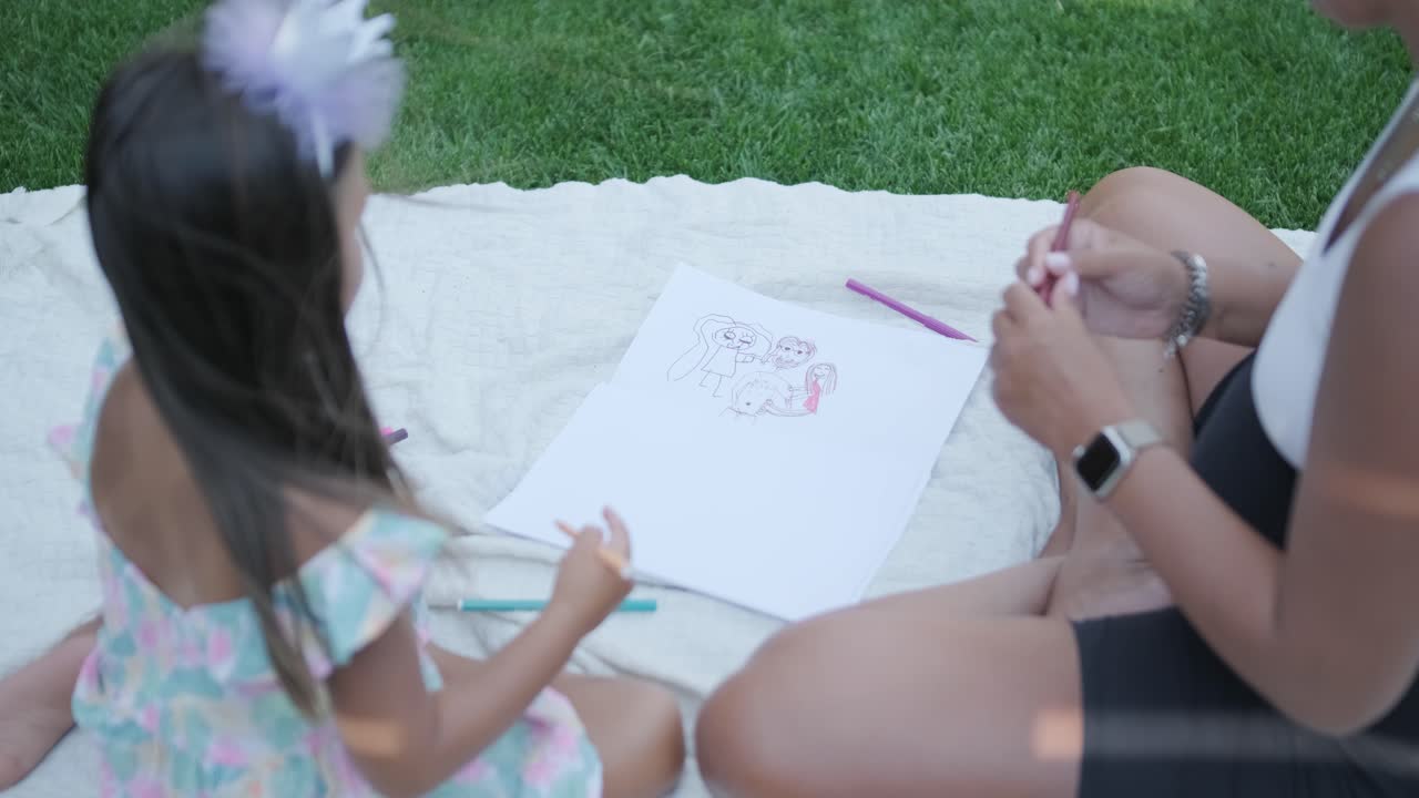 una madre y su hija pequeña se sientan en una manta en el patio trasero, participando en una actividad de dibujo juntos. la escena al aire libre captura un momento familiar pacífico, fomentando la creatividad y el vínculo.
