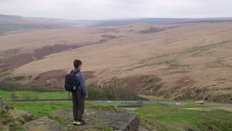 Young-boy-outdoors-standing-on-a-countryside-hill-top,-admiring-the-moorland-views