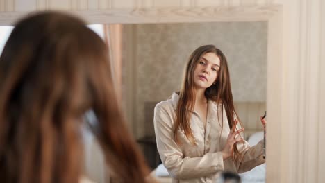 retrato de primer plano de una mujer hermosa joven en el espejo aplica spray para el cabello