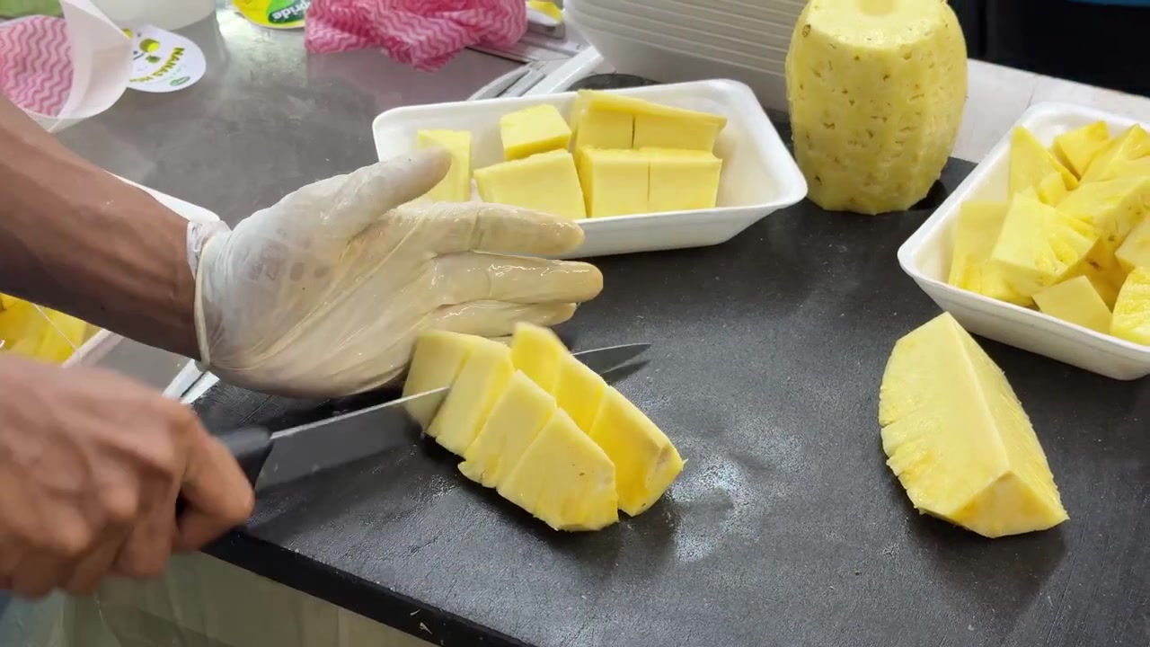 Worker Slicing Fresh Pineapple into Pieces on Cutting Board